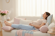 Crie uma imagem de uma mulher grávida relaxando em um sofá ou cama, com um cinto de sustentação abdominal que proporciona alívio. Ela deve estar com uma expressão de relaxamento e conforto, com as pernas esticadas e um ambiente tranquilo ao redor. A paleta de cores deve continuar suave, com tons de rosa claro e azul clarinho, transmitindo calma e bem-estar.